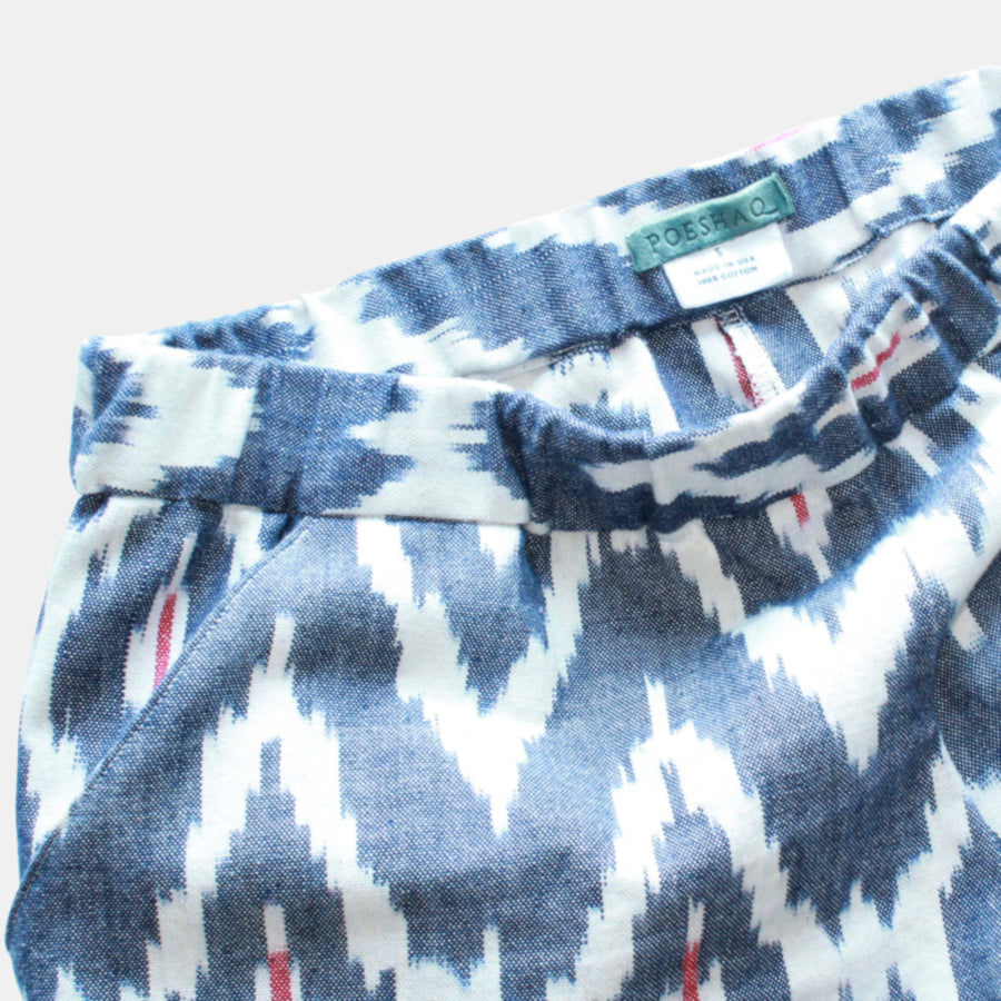 Flat lay close up view of Terra Tapered Pant in Ikat Cotton. The pant has an elastic waist and cuffs with front side pockets. Color and pattern of the fabric is denim chevron with hints of red.