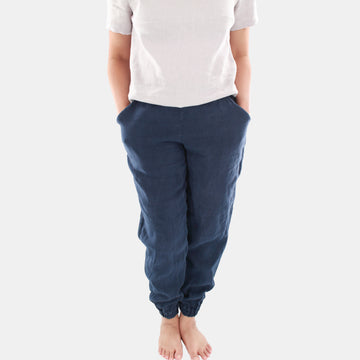 Close up of a female model wearing Terra Tapered Pant in Midweight Linen. The pant has an elastic waist and cuffs with front side pockets. Color of the fabric is navy.