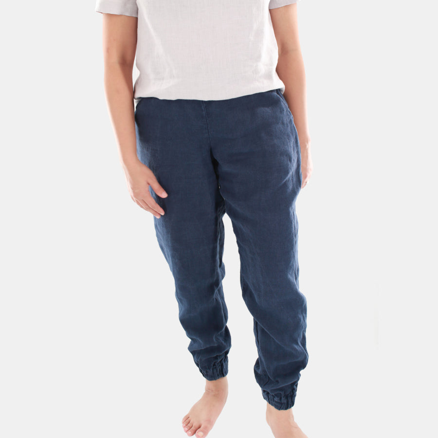 Female model wearing Terra Tapered Pant in Midweight Linen. The pant has an elastic waist and cuffs with front side pockets. Color of the fabric is navy.