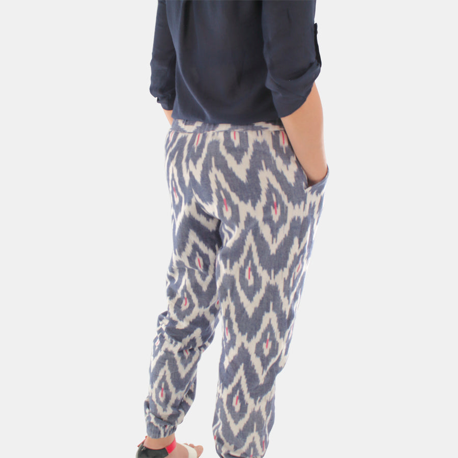 Back view of a female model wearing Terra Tapered Pant in Ikat Cotton. The pant has an elastic waist and cuffs with front side pockets. Color and pattern of the fabric is denim chevron with hints of red.