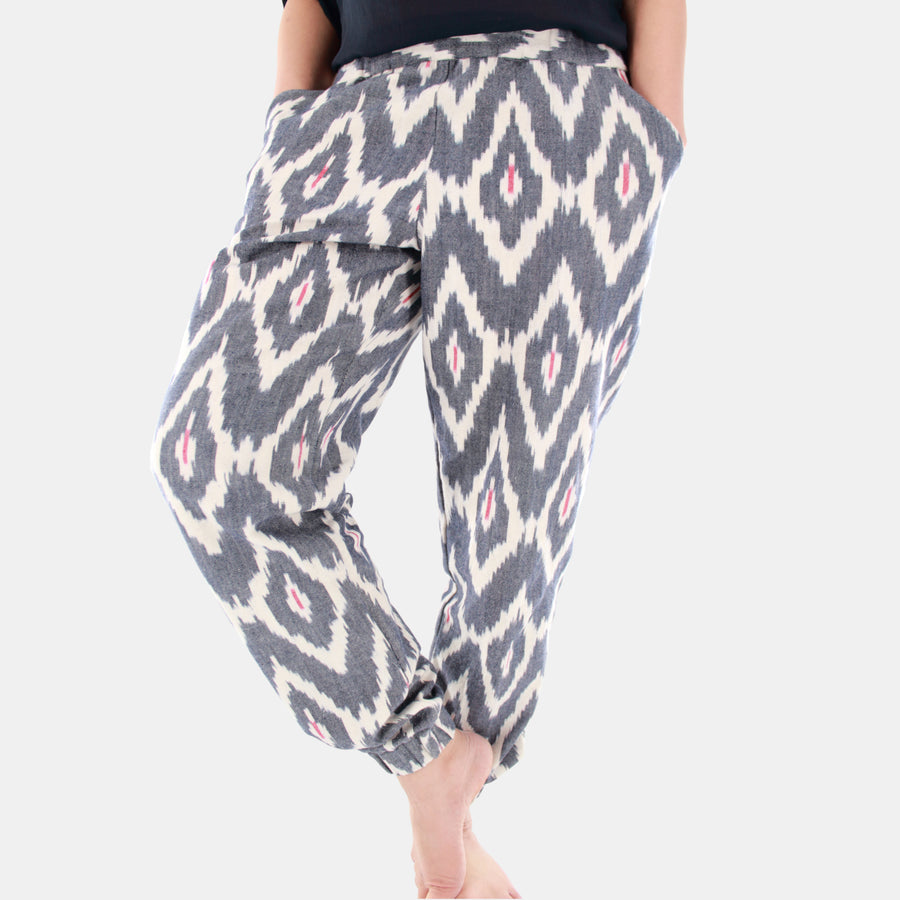 Female model wearing Terra Tapered Pant in Ikat Cotton. The pant has an elastic waist and cuffs with front side pockets. Color and pattern of the fabric is denim chevron with hints of red.