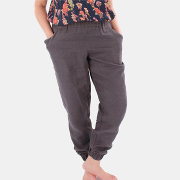 Close up of a female model wearing Terra Tapered Pant in Midweight Linen. The pant has an elastic waist and cuffs with front side pockets. Color of the fabric is anthracite grey.