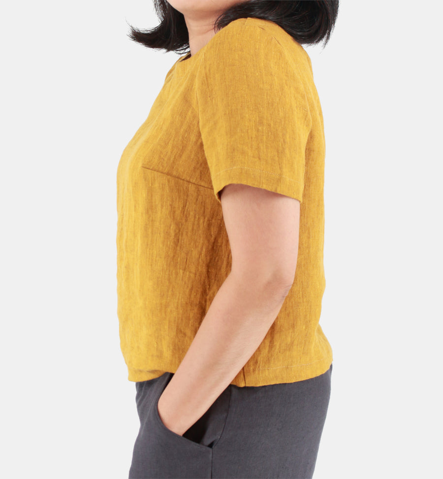 Side view of a female model wearing womens crop top in Midweight Linen. Color of the top is rich mustard with hints of brown.
