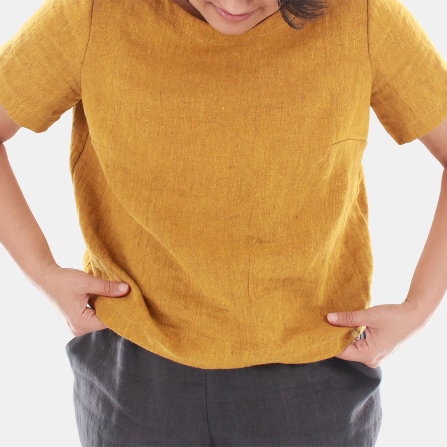 Front close up of a female model wearing womens crop top in Midweight Linen. Color of the top is rich mustard with hints of brown.
