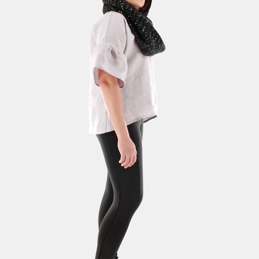 Side view of a female model wearing womens willow bell sleeve top in Midweight Linen. Accessorized with black infinity scarf. High-low hem finishing from front to back. Color of the top is snow grey.