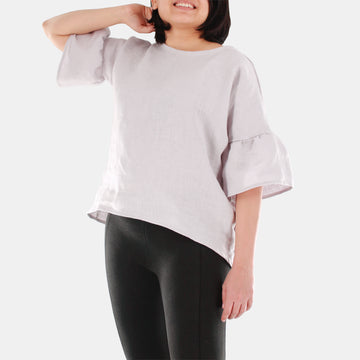 Smiling female model wearing womens willow bell sleeve top in Midweight Linen. High-low hem finishing from front to back. Color of the top is snow grey.