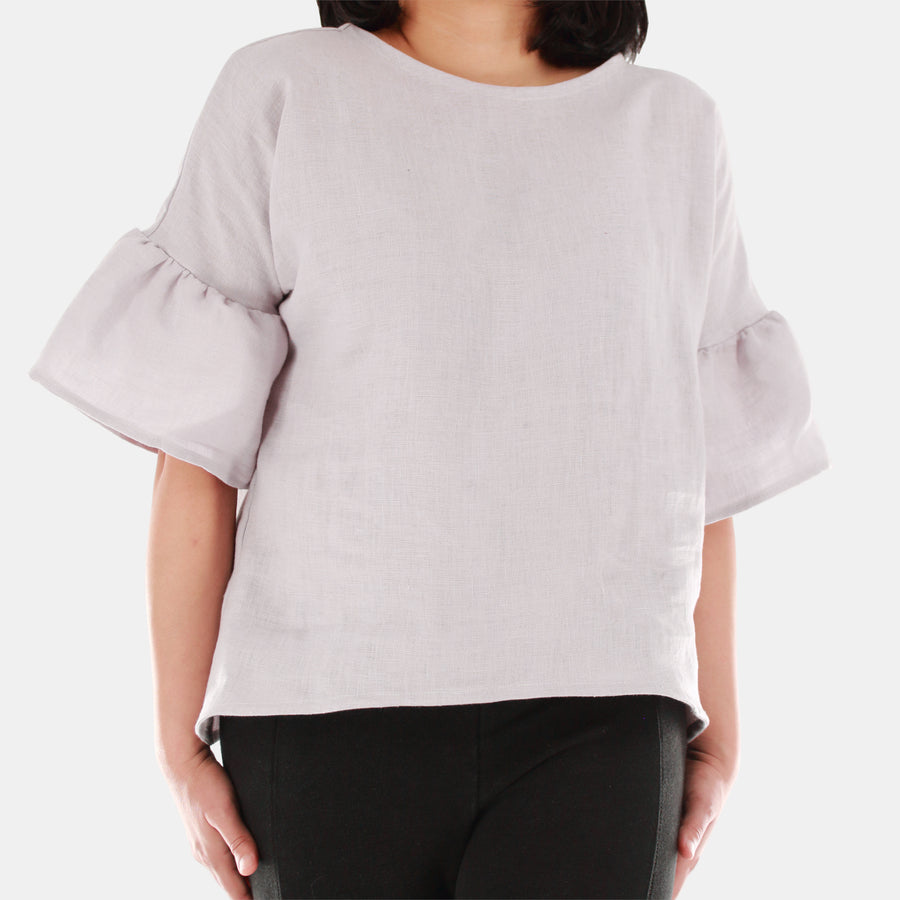 Front close up of a female model wearing womens willow bell sleeve top in Midweight Linen. High-low hem finishing from front to back. Color of the top is snow grey.
